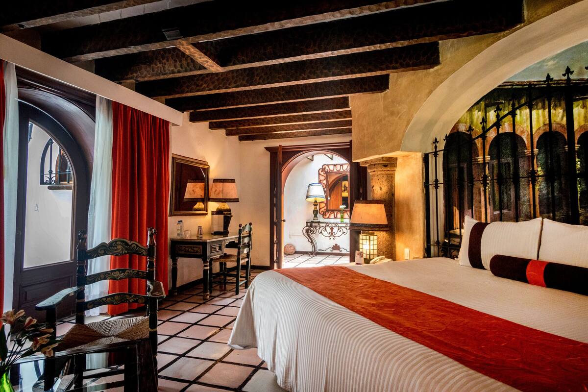 Habitación de hotel con una cama grande, un escritorio y una silla. Cuenta con una ventana con cortinas, una puerta y vistas al exterior.