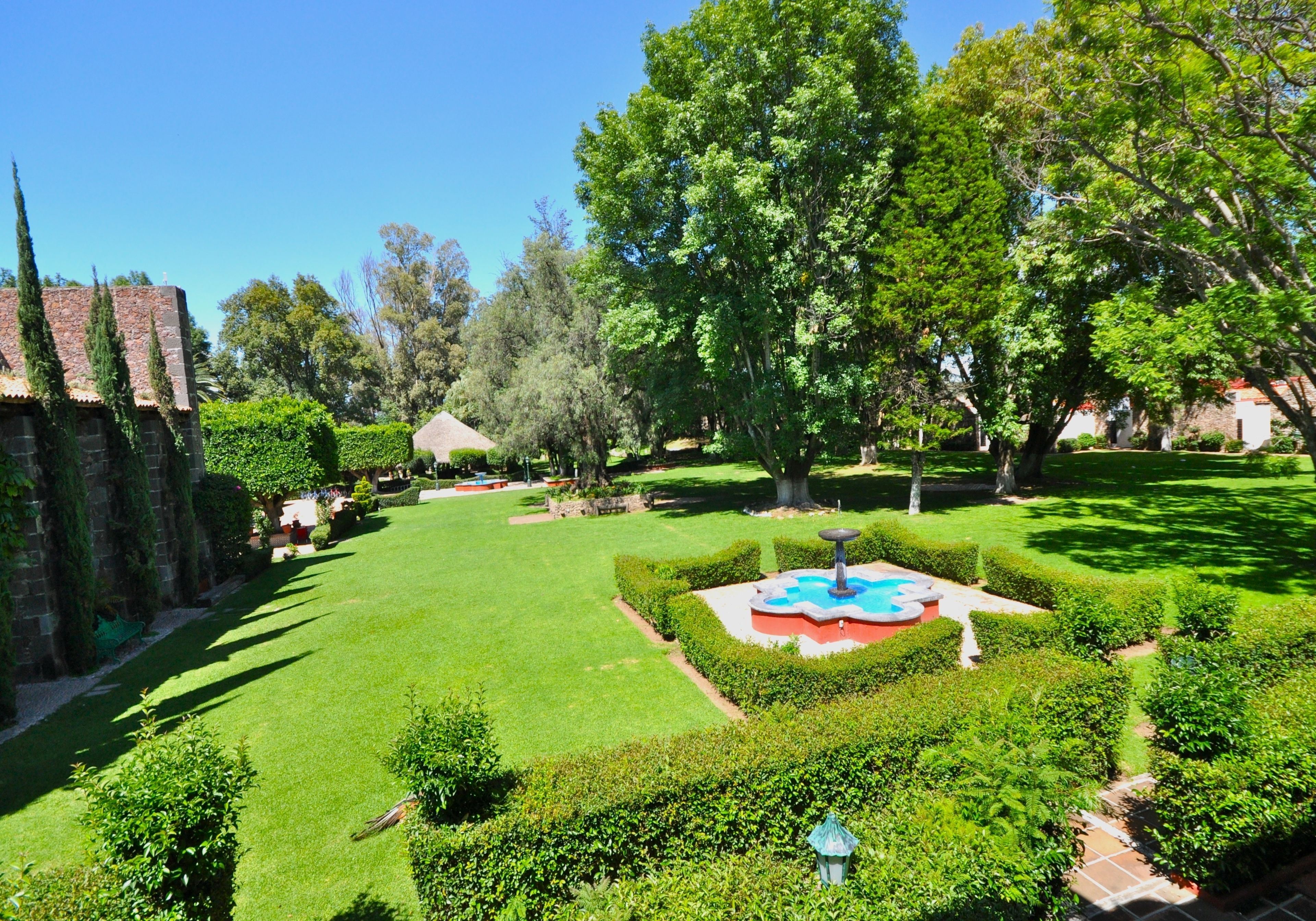 A well-maintained garden with a fountain, neatly trimmed hedges, and a variety of trees.
