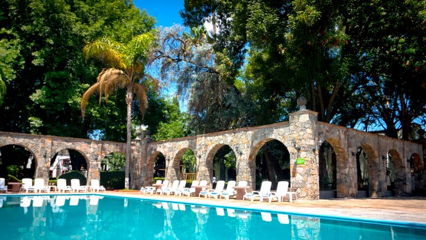 Una piscina con sillas reclinables blancas y arcos de piedra.