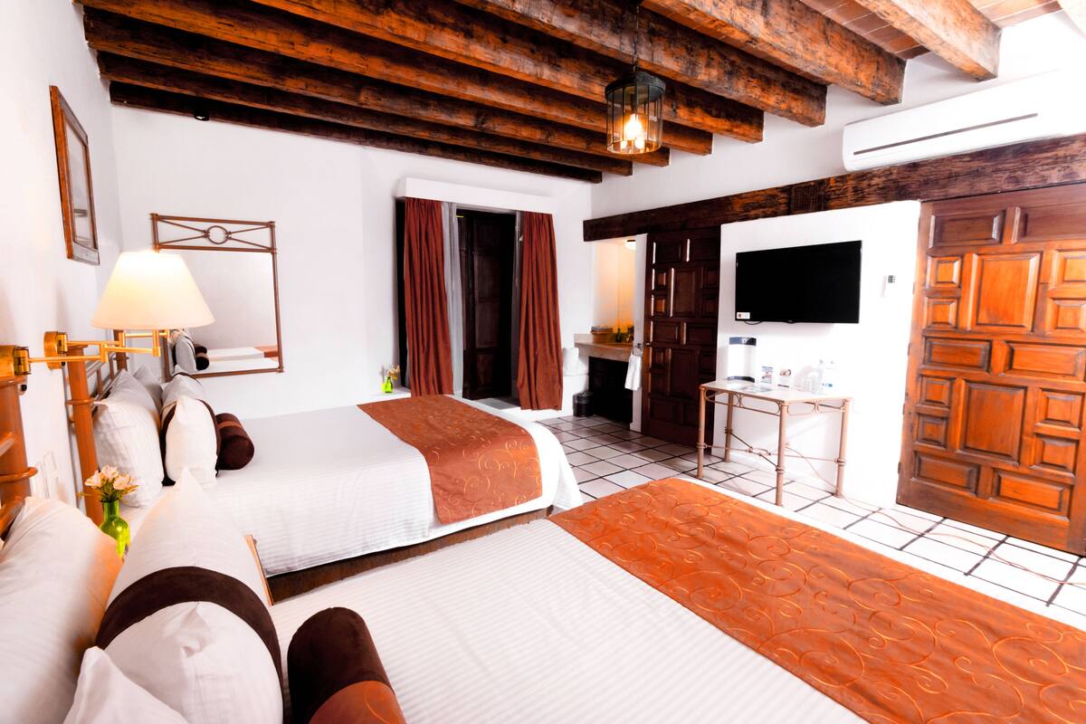 Habitación de hotel con dos camas, televisor, escritorio y baño con ducha e inodoro.