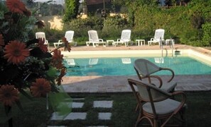 Una piscina con sillas de descanso blancas y una silla de mimbre al frente.