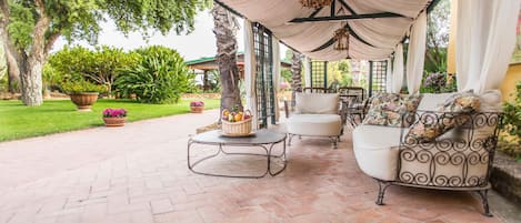 Un patio cubierto con mobiliario exterior, una mesa con una cesta de frutas y plantas en macetas.