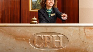 A receptionist at a hotel reception desk with a nameplate and a bell.