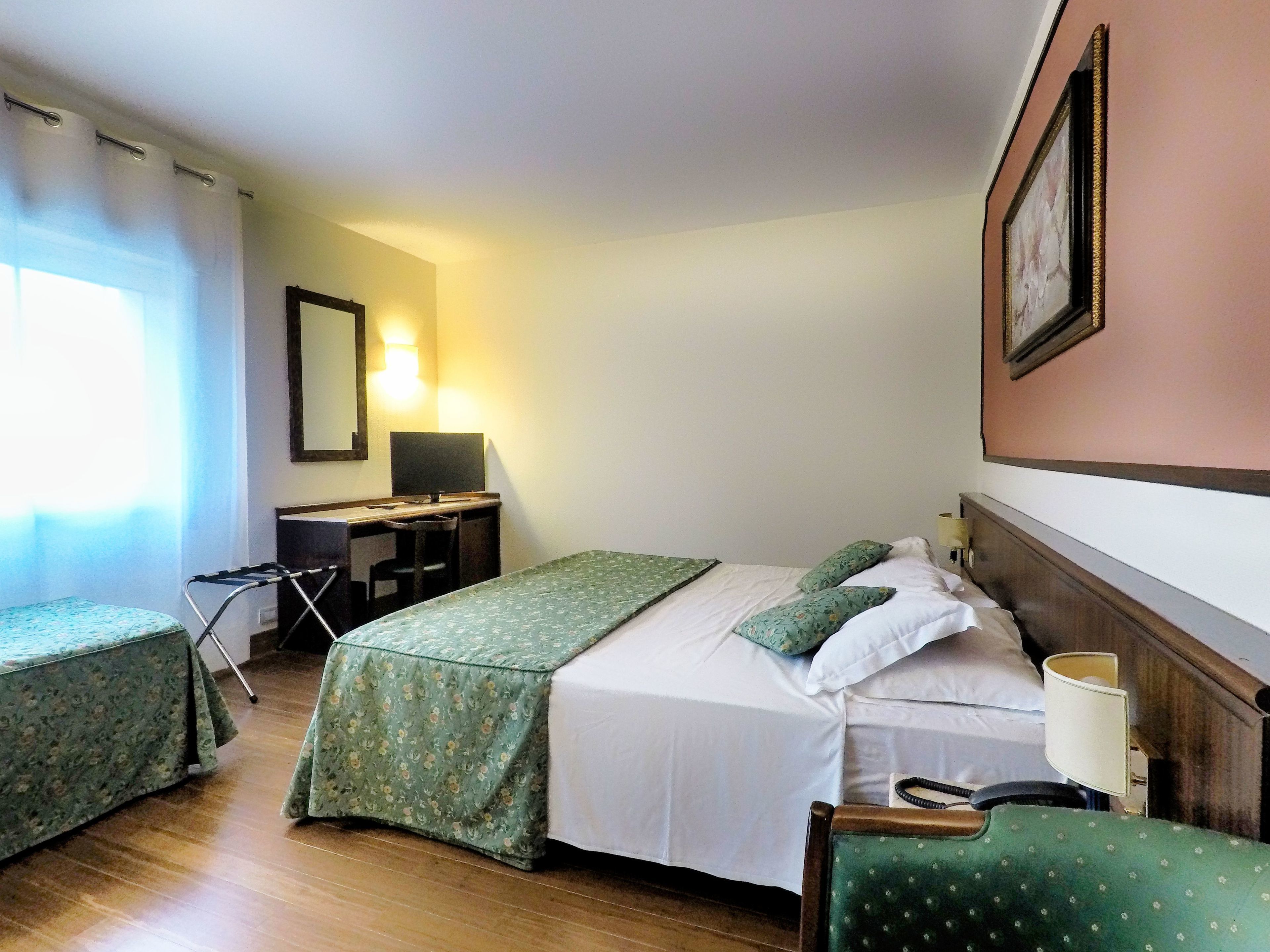 Een hotelkamer met twee eenpersoonsbedden, een bureau met stoel, een spiegel en een lamp.