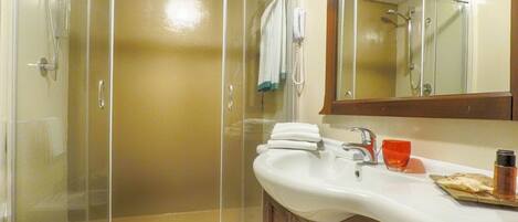 Un baño con ducha de vidrio, un lavamanos blanco con un jabonera roja y un tocador de madera.
