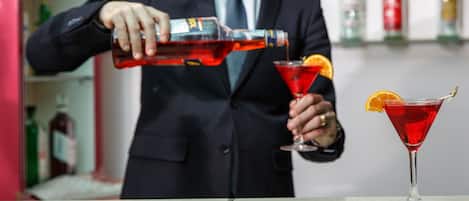 A person pouring a red liquid into a martini glass with an orange slice garnish.
