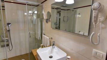 A modern bathroom with a glass-enclosed shower, a sink with a mirror above it, and a hairdryer mounted on the wall.
