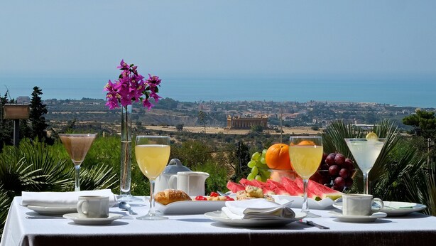 A table set with a meal and drinks overlooking a scenic view of a coastal town.