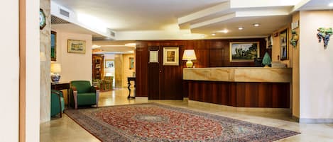 A spacious lobby with a large, ornate carpet, a reception desk, and a seating area with chairs.