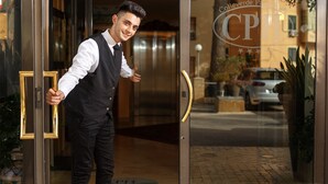 A man in a vest and tie standing at a hotel entrance with a visible sign reading "Colleverde Park" and "CPD".