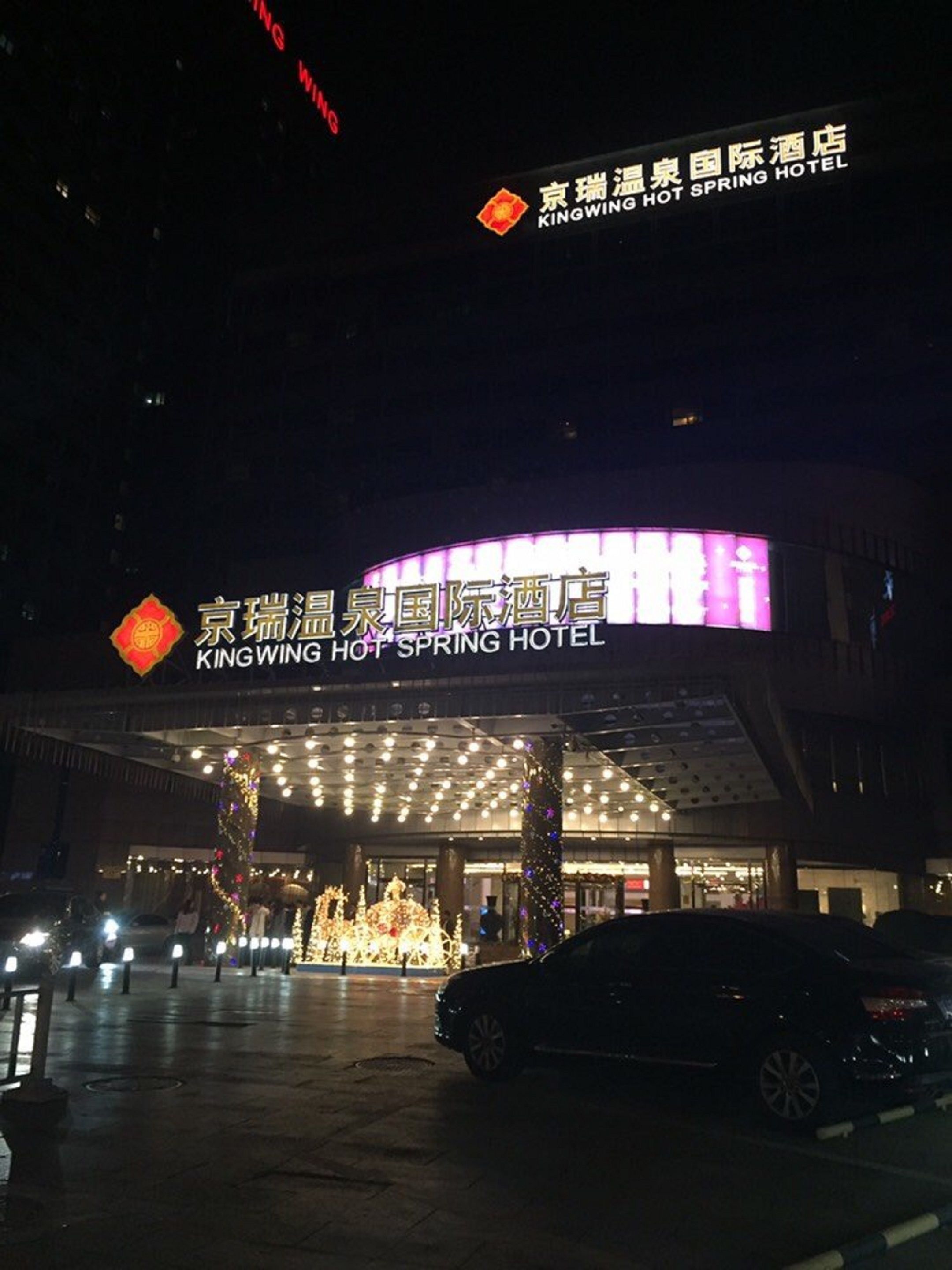 The exterior of the King Wing Hot Spring Hotel with illuminated signage and a covered entrance area.