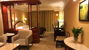 Une chambre d’hôtel avec un lit, un bureau, une chaise, une petite table, une plante et un grand miroir.
