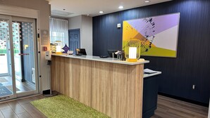 A reception area with a wooden reception desk, a green rug, and a wall-mounted abstract art piece. - Spark by Hilton Guilford (Guilford)