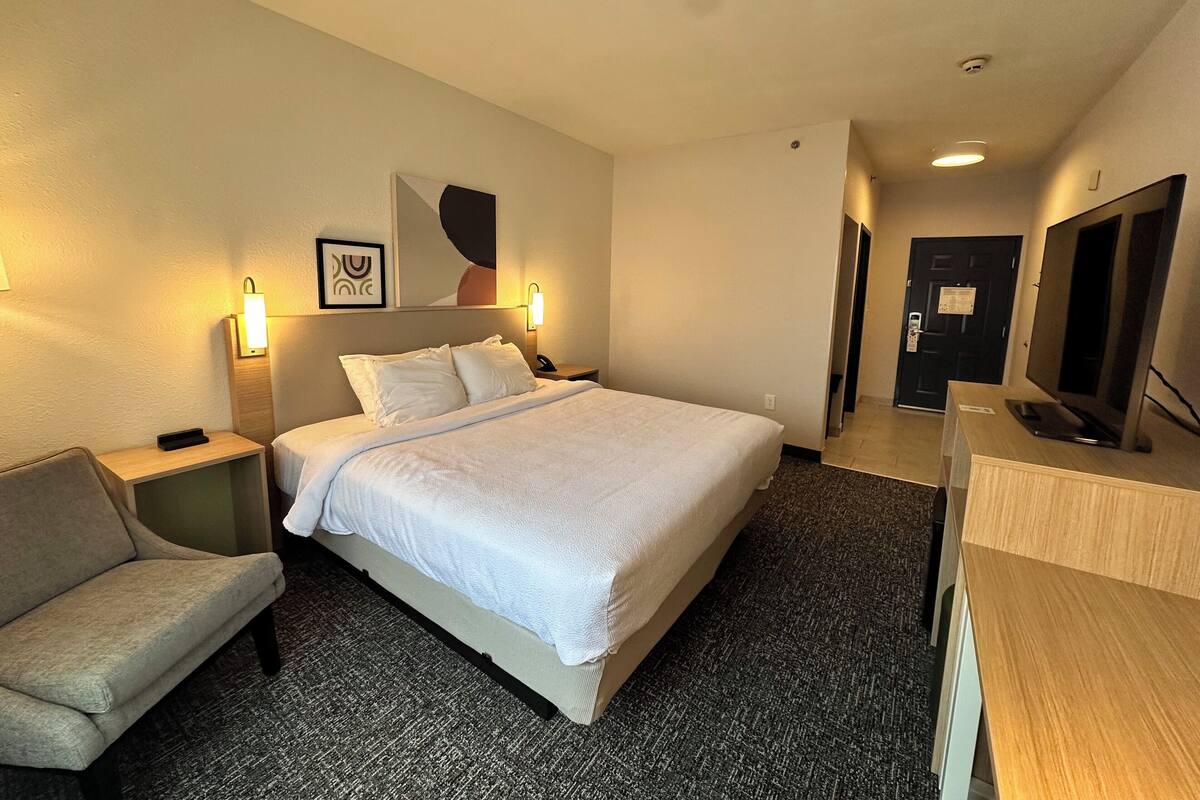 A hotel room with a bed, a desk, a chair, a TV, and a door.