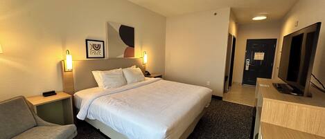 Een hotelkamer met een bed, een bureau, een stoel, een televisie en een deur.
