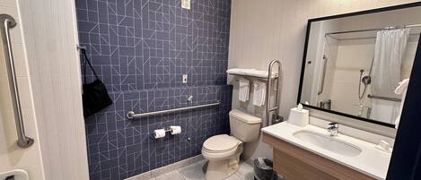 A modern bathroom with a geometric tile backsplash, a toilet, a sink with a mirror, and a grab bar.