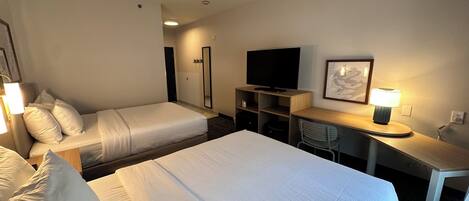 A hotel room with two beds, a desk, a chair, a television, and a lamp.