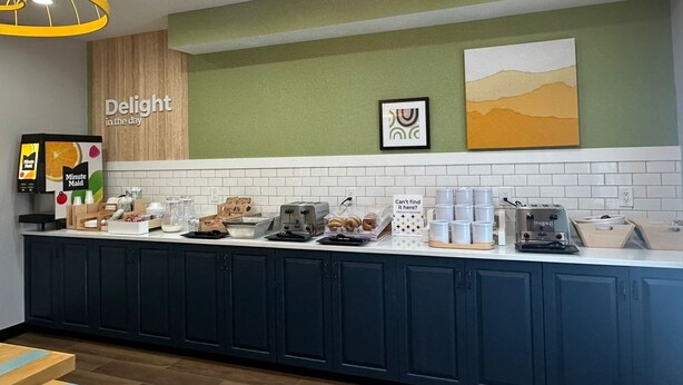 A modern kitchen area with a long counter, various appliances, and a sign that reads "Delight in the day". - Spark by Hilton Guilford (Guilford)