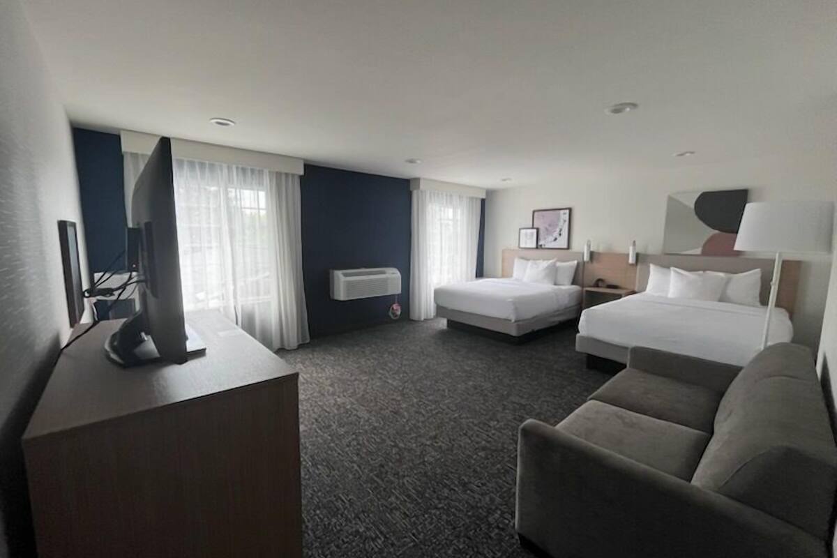 A hotel room with a large bed, a smaller bed, a desk with a computer, and a couch.