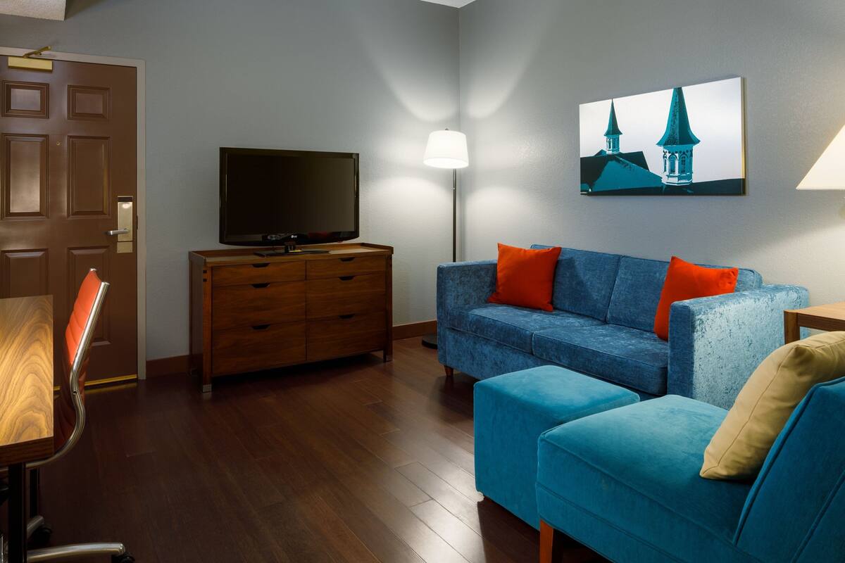 A modern living room with a blue sofa, wooden TV stand, and a painting of a church on the wall.