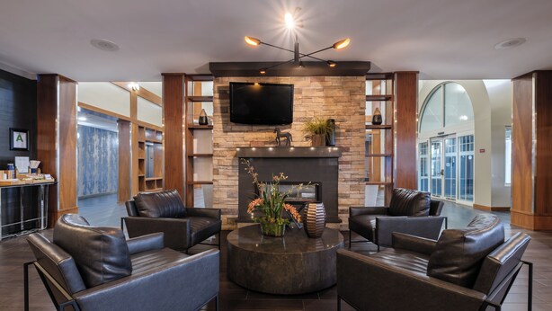 A modern lobby with leather sofas, a stone fireplace, and a flat-screen TV mounted on the wall. - Four Points by Sheraton Louisville Airport (Louisville)