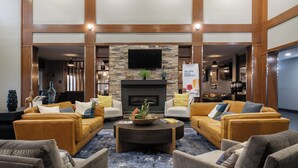 A spacious living area with a fireplace, comfortable seating, and a flat-screen TV mounted above it. - Four Points by Sheraton Louisville Airport (Louisville)