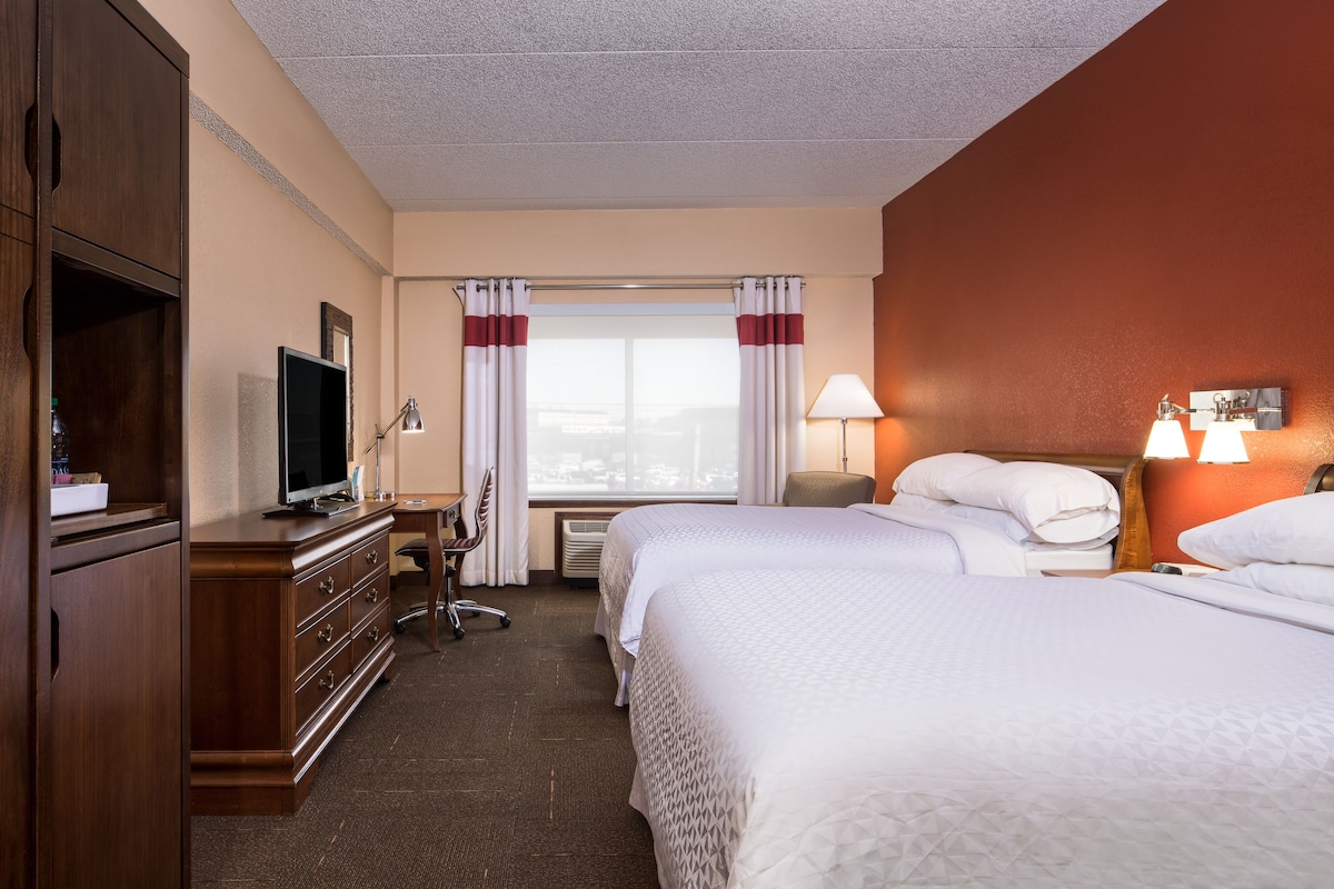 A hotel room with two beds, a TV, a desk, and a dresser.
