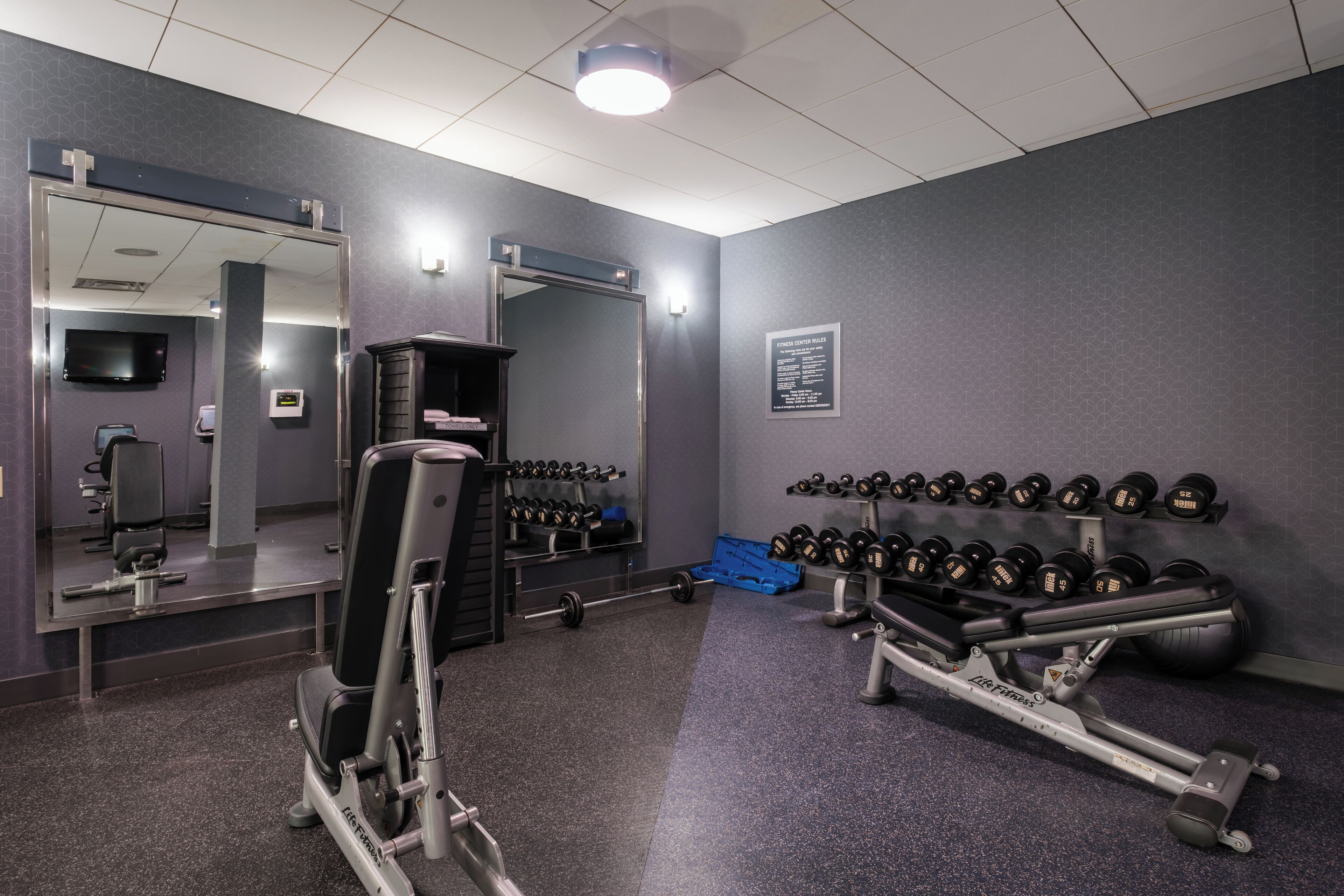 Ett gym med utrustning för styrketräning, speglar och hantlar.