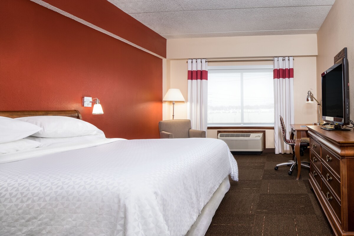 A hotel room with a large bed, a desk, a television, a lamp, and a window with curtains.