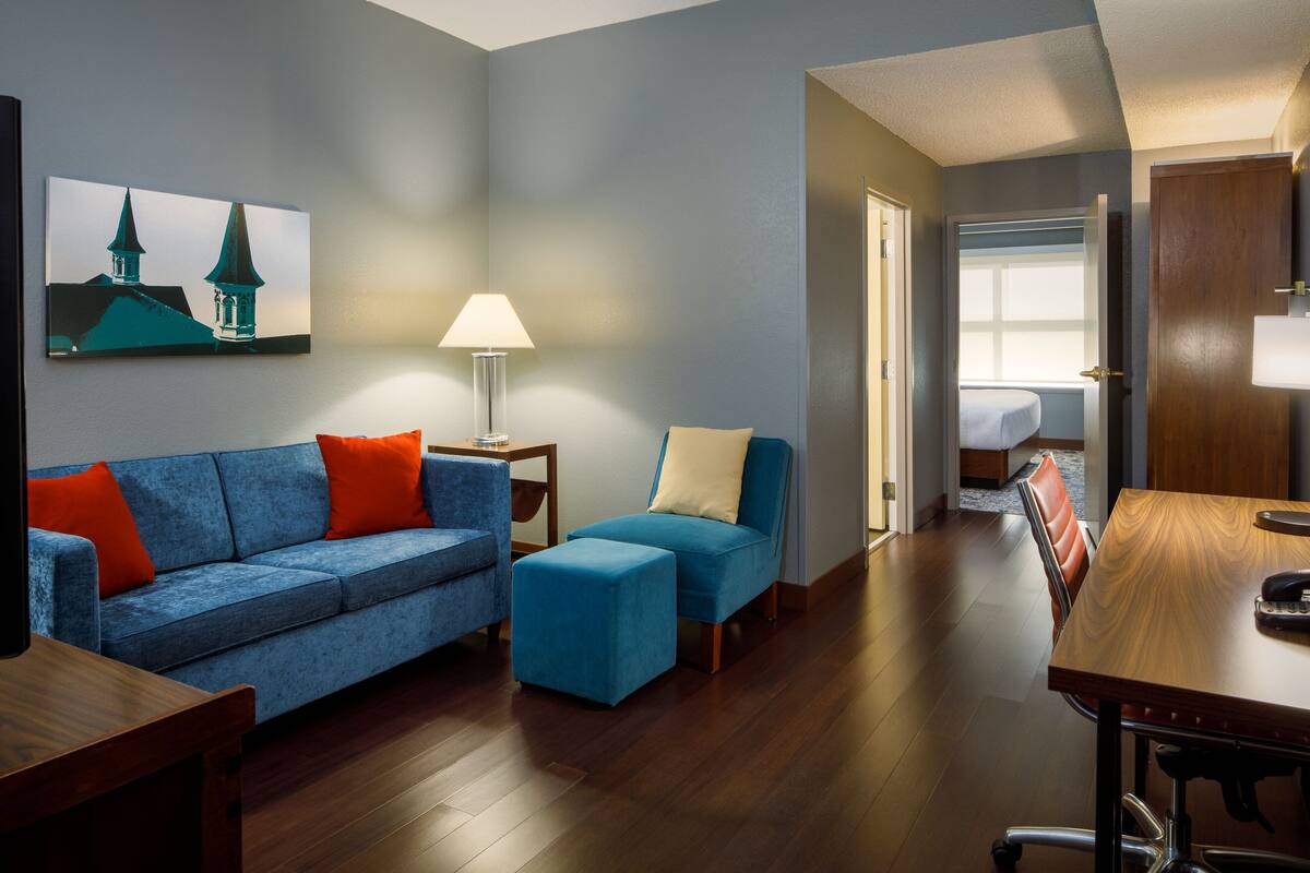 A modern living room with a blue sofa, ottoman, and a wooden dining table.