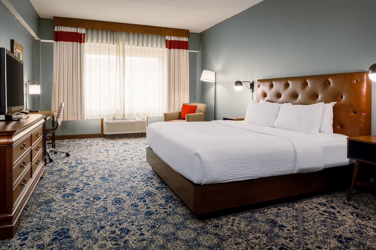 A hotel room with a large bed, a desk, a chair, a dresser, and a television.