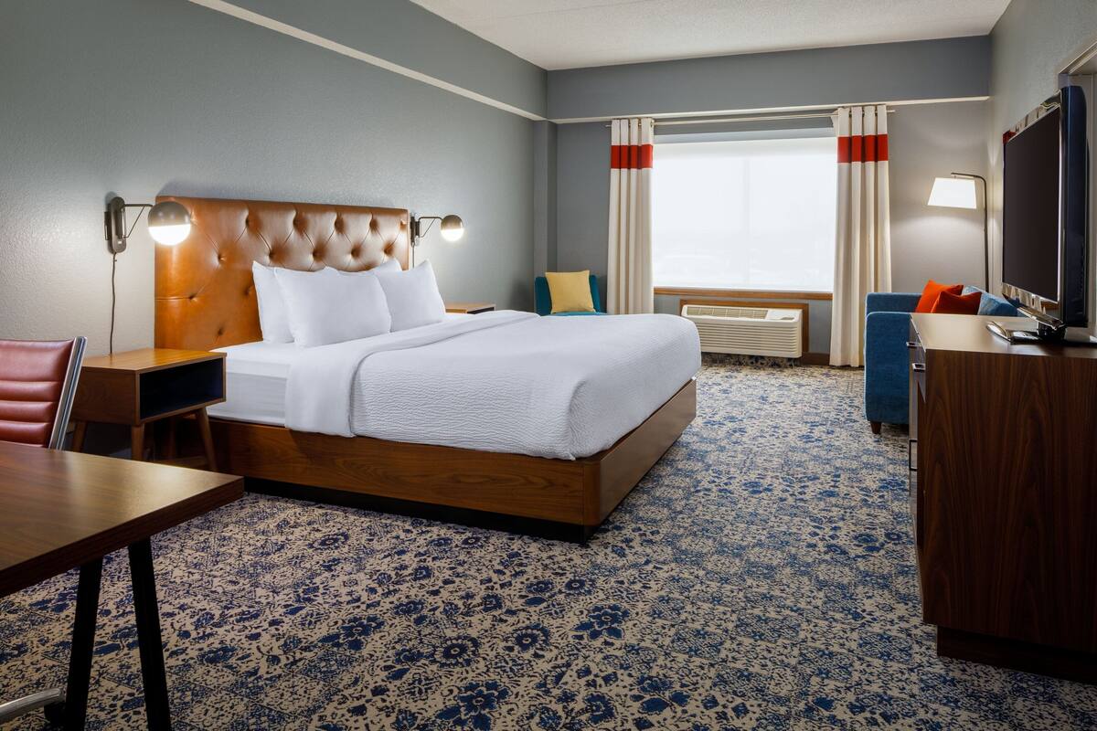 A hotel room with a large bed, a desk, a chair, a TV, and a window with curtains.