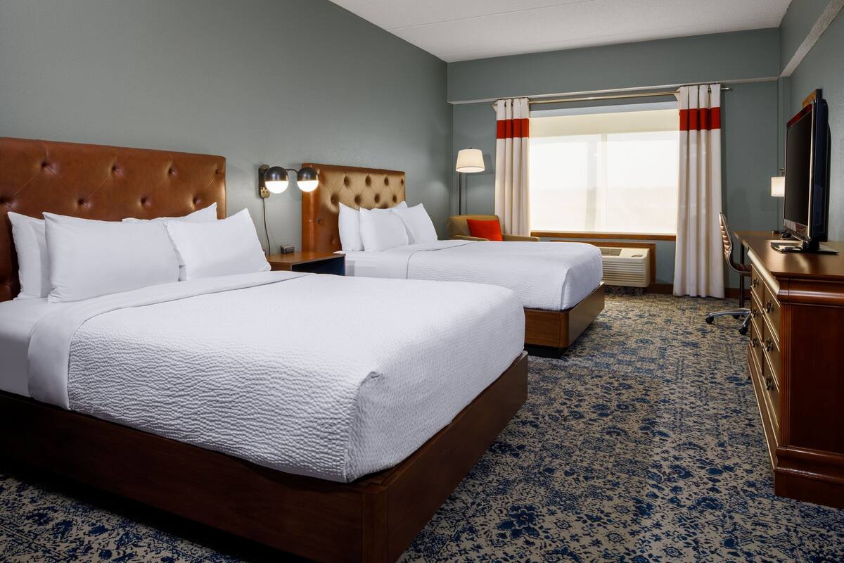 A hotel room with two beds, a television, a desk, and a window with curtains.