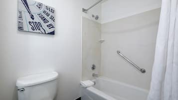 A bathroom with a toilet, a shower with a grab bar, and a wall-mounted artwork.