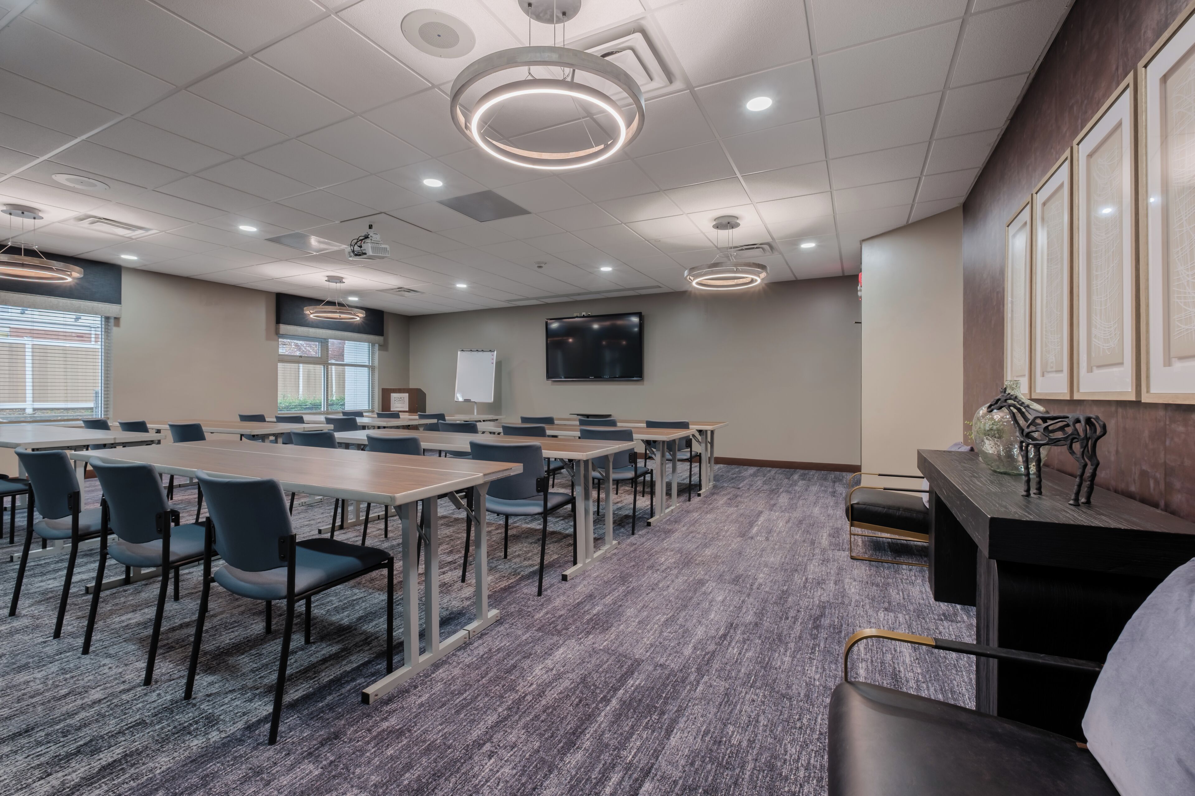 A conference room with a long table, chairs, a projector, a TV, and framed artwork on the wall.