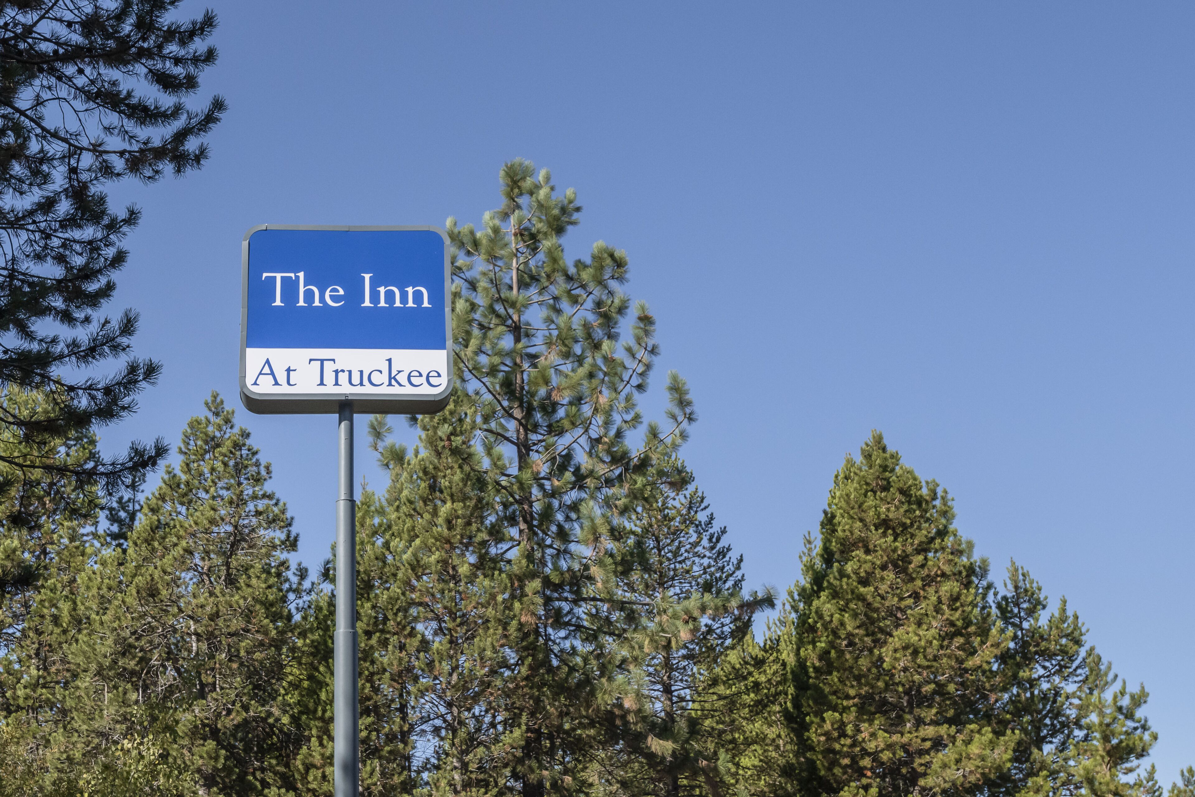 Señal de 'The Inn At Truckee' con un cielo azul despejado y pinos al fondo.