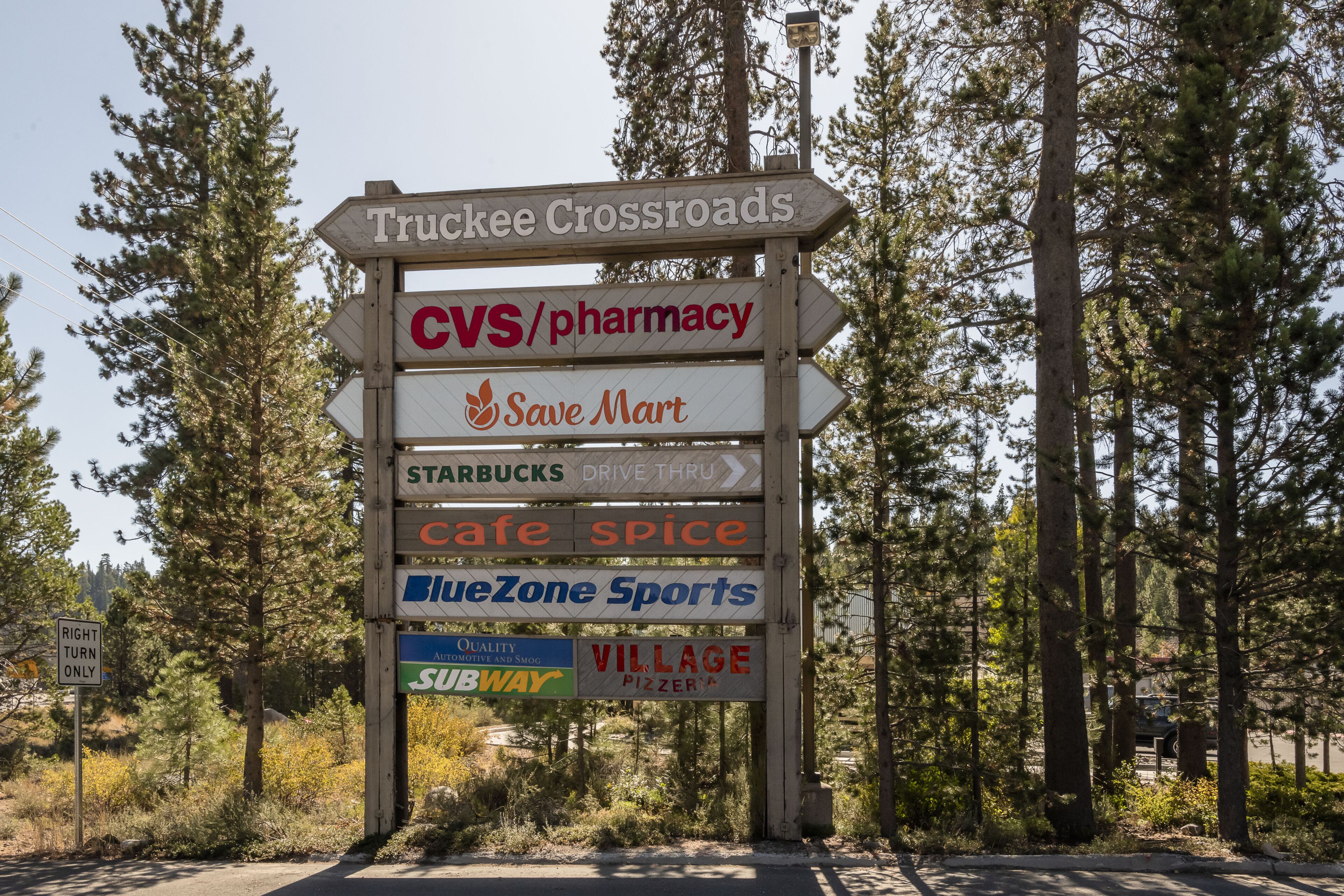 A signpost with multiple business names including CVS/pharmacy, Save Mart, Starbucks, Cafe Spice, BlueZone Sports, Subway, and Village Pizza.