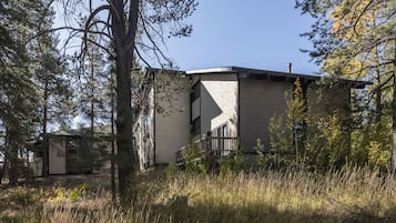 Een gebouw met twee verdiepingen en een balkon, omringd door hoge bomen en gras.