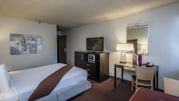A hotel room with a bed, a desk with a chair, a television, a desk lamp, and a mirror.