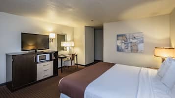 A hotel room with a bed, a desk with a chair, a television, a microwave, a lamp, and a painting on the wall.
