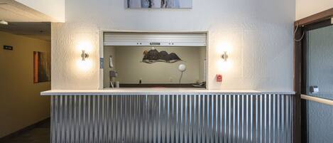 A reception desk with a corrugated metal barrier, two wall-mounted light fixtures, and a framed artwork above.