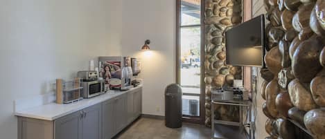 A kitchen with a stone wall, a microwave, a coffee maker, and a trash can.