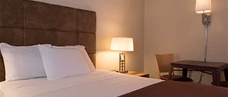 A hotel room with a large bed, a nightstand with a lamp, a chair, and a small table.