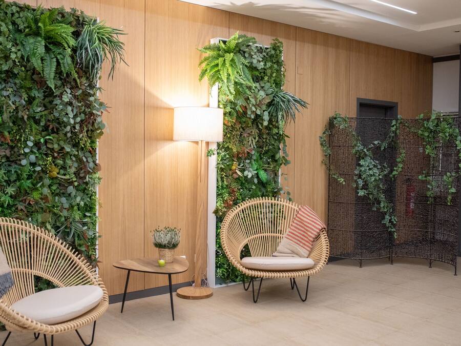 Une pièce comprenant deux fauteuils en osier, une petite table ronde et une lampe. Les murs sont décorés de jardins verticaux.