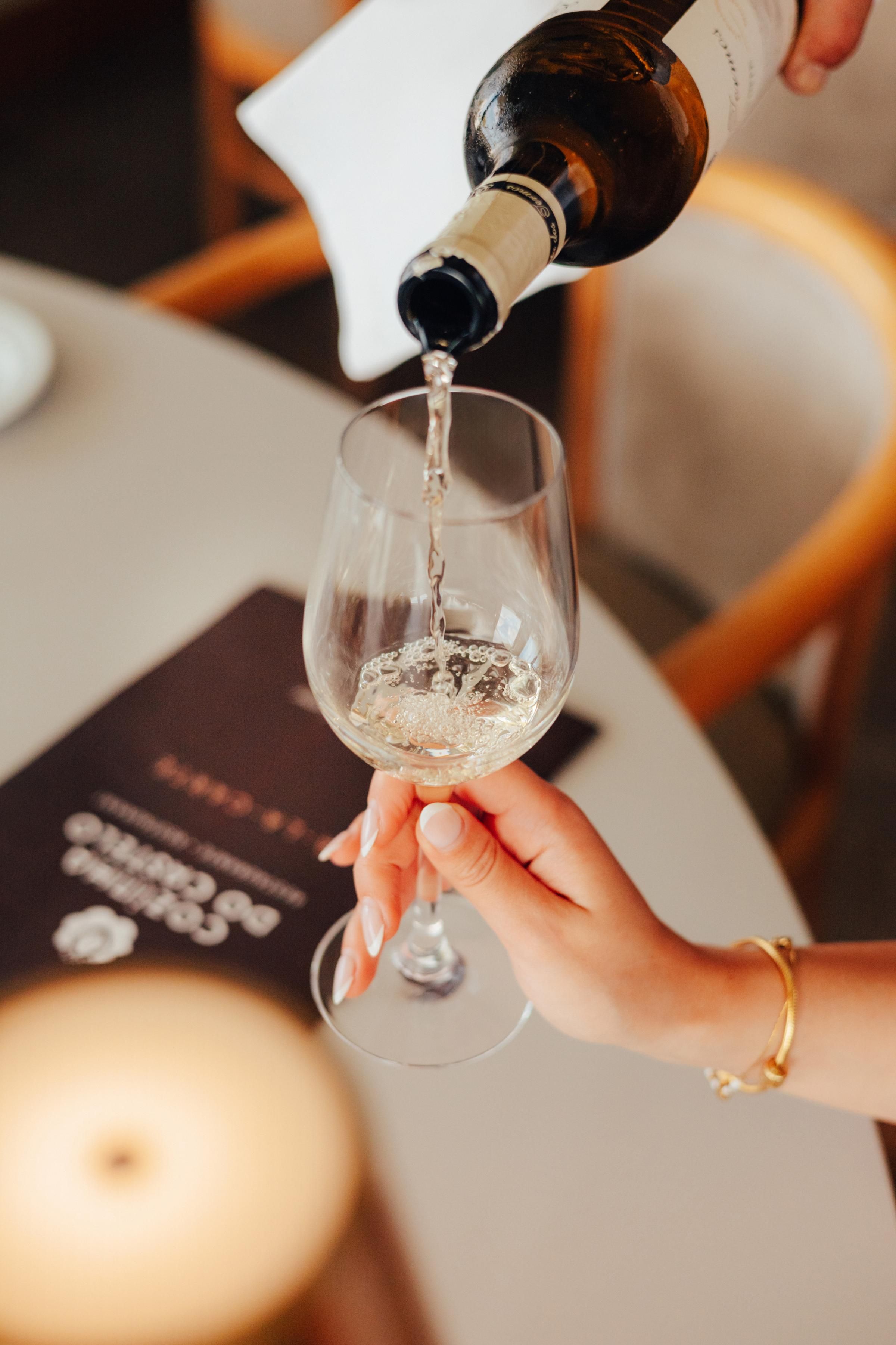 A hand holding a wine glass with a bottle pouring wine into it.