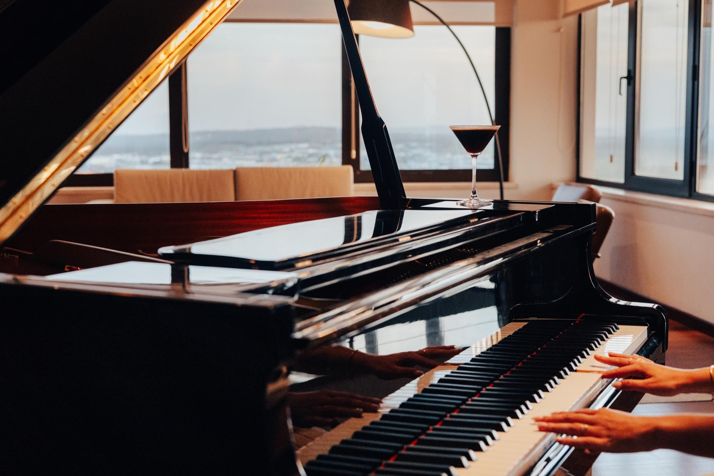 A grand piano in a room with large windows, a lamp, and a book on the piano.