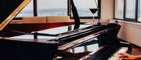 Un piano de cola en una habitación con ventanas amplias, una lámpara y un libro sobre el piano.