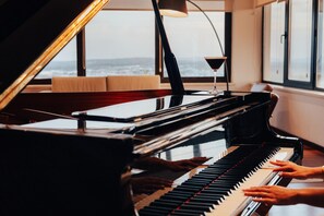 Un piano de cola en una habitación con ventanas amplias, una lámpara y un libro sobre el piano.