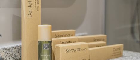 A bathroom counter with a dental kit, a bottle of shampoo, and several boxes labeled with different product names.