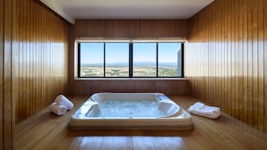 A wooden-paneled room with a large window, a hot tub, and towels on the floor. - Melia Castelo Branco (Castelo Branco)